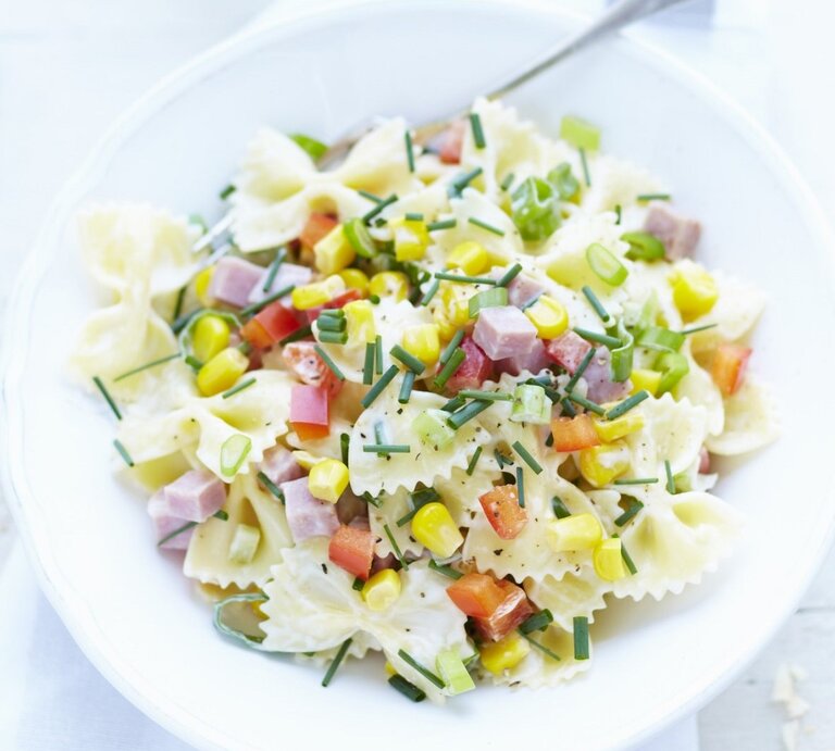 In einer Schüssel ist eine Portion Nudelsalat mit Farfalle, Schinkenwürfeln und Mais angerichtet. | © StockFood / PhotoCuisine / Chivoret