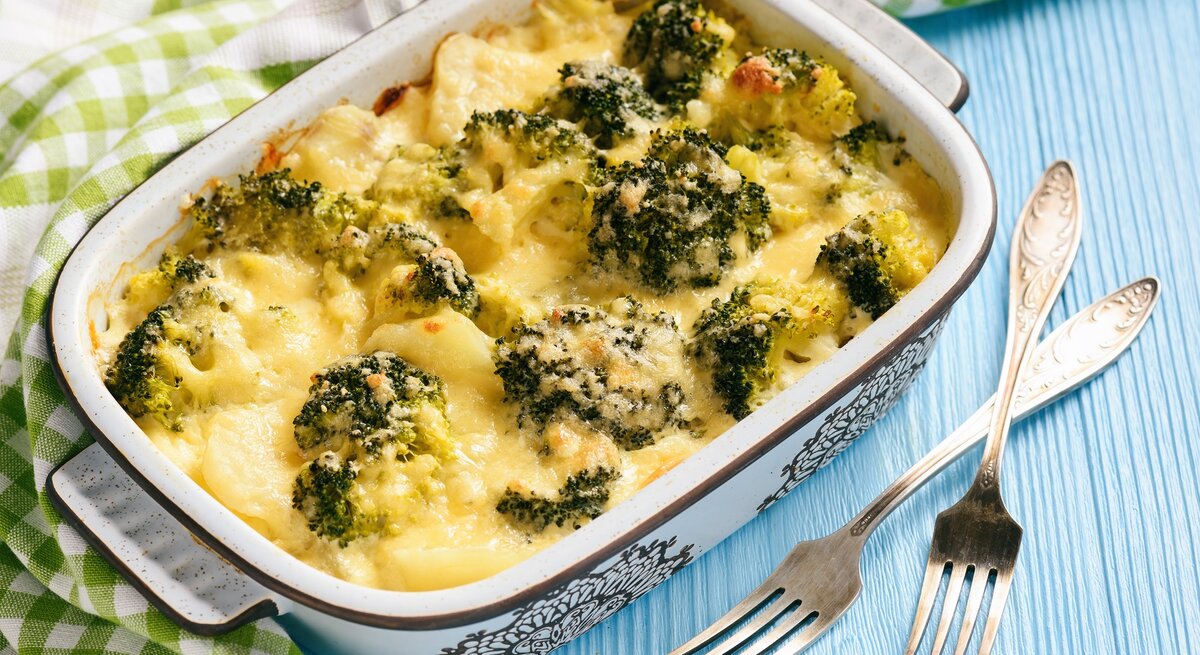Eine Ofenform mit Kohlrabi-Brokkoli-Auflauf, überbacken mit Käse, daneben liegen ein Geschirrtuch und zwei Gabeln.
