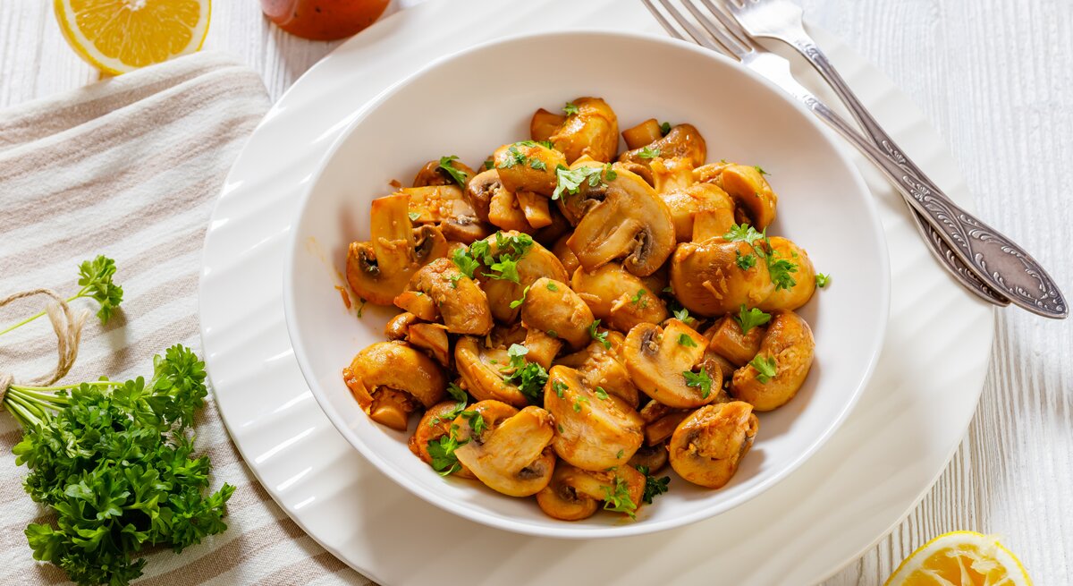 Spanische Knoblauch-Champignons in weißer Schale auf weißem Holz. 