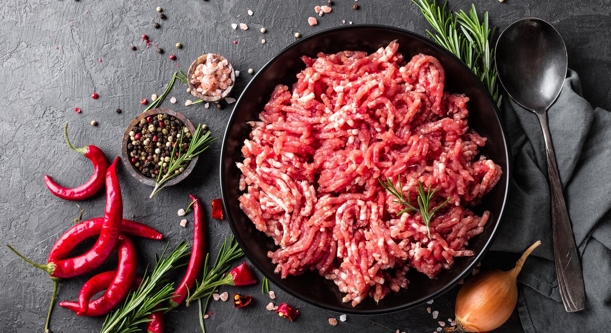 Rohes Hackfleisch auf einem schwarzen Teller. Daneben mehrere verschiedene Gewürze. 