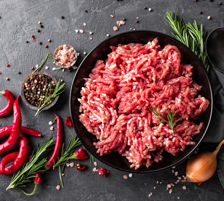 Rohes Hackfleisch auf einem schwarzen Teller. Daneben mehrere verschiedene Gewürze.  | © iStock/YelenaYemchuk