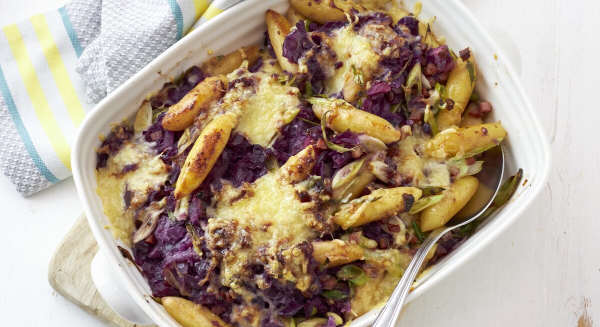 Rotkohl-Schupfnudel-Gratin mit Speck, serviert in einer hellen Auflaufform auf weißem Untergrund.
