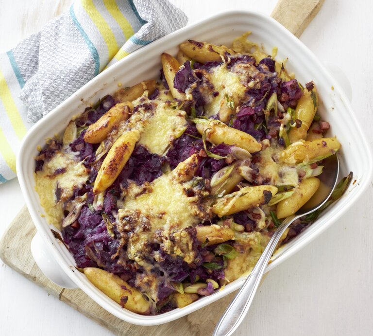 Rotkohl-Schupfnudel-Gratin mit Speck, serviert in einer hellen Auflaufform auf weißem Untergrund. | © StockFood / StockFood Studios / Brachat, Oliver