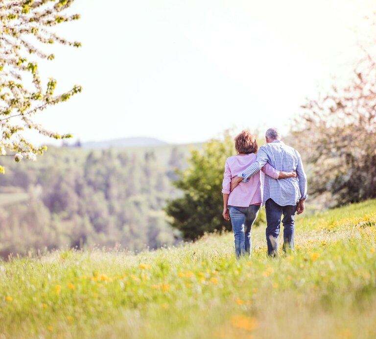 Rückansicht auf ein Pärchen, das auf einer Wiese spazieren geht. | © iStock.com/Halfpoint