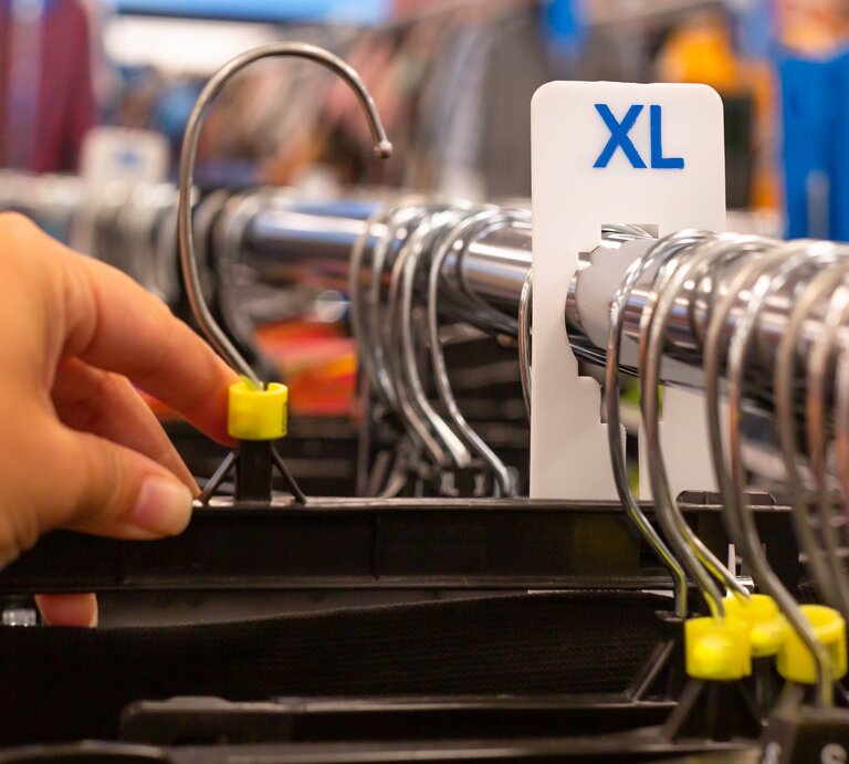 Kleiderbügel auf einer Kleiderstange, ein XL-Zeichen ist an der Stange angebracht | © Getty Images /	globalmoments