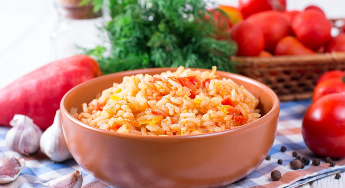 Eine Schale griechischer Tomatenreis mit Paprika, drumherum die frischen Zutaten.