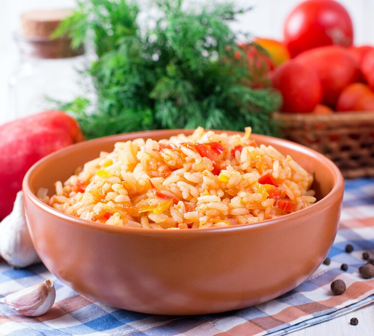 Eine Schale griechischer Tomatenreis mit Paprika, drumherum die frischen Zutaten. | © Adobe Stock/ qwartm