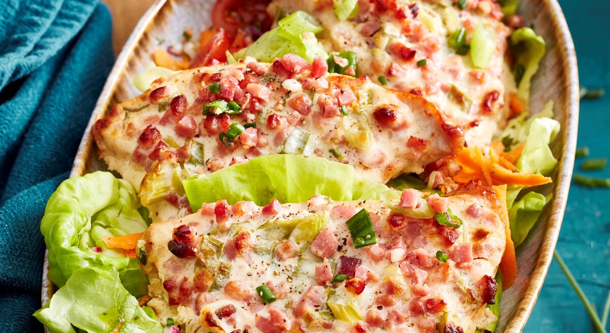 Flammkuchen-Schnitzel mit Salatblättern in einer Schale vor Hintergrund mit blauem Stoff. 