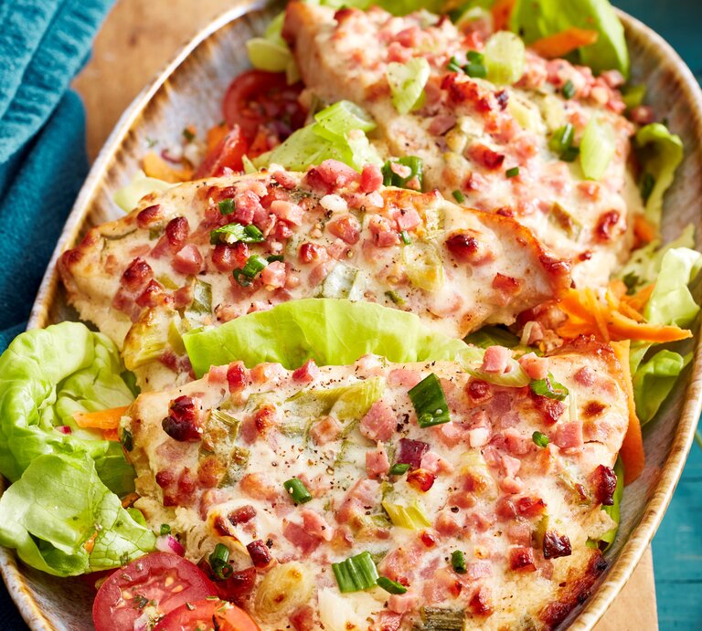 Flammkuchen-Schnitzel mit Salatblättern in einer Schale vor Hintergrund mit blauem Stoff.  | © EAT CLUB / Isabell Triemer