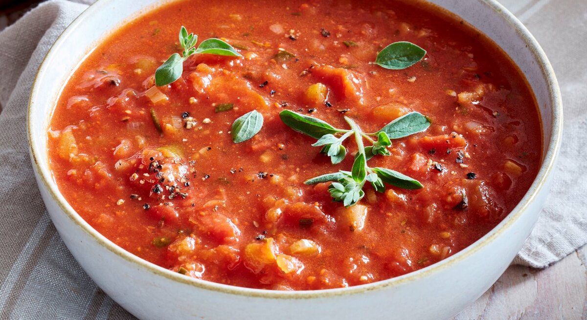 In einer Schüssel ist eine Portion feurige Tomatensuppe mit Rosmarin angerichtet. Sie ist mit Basilikum verfeinert.