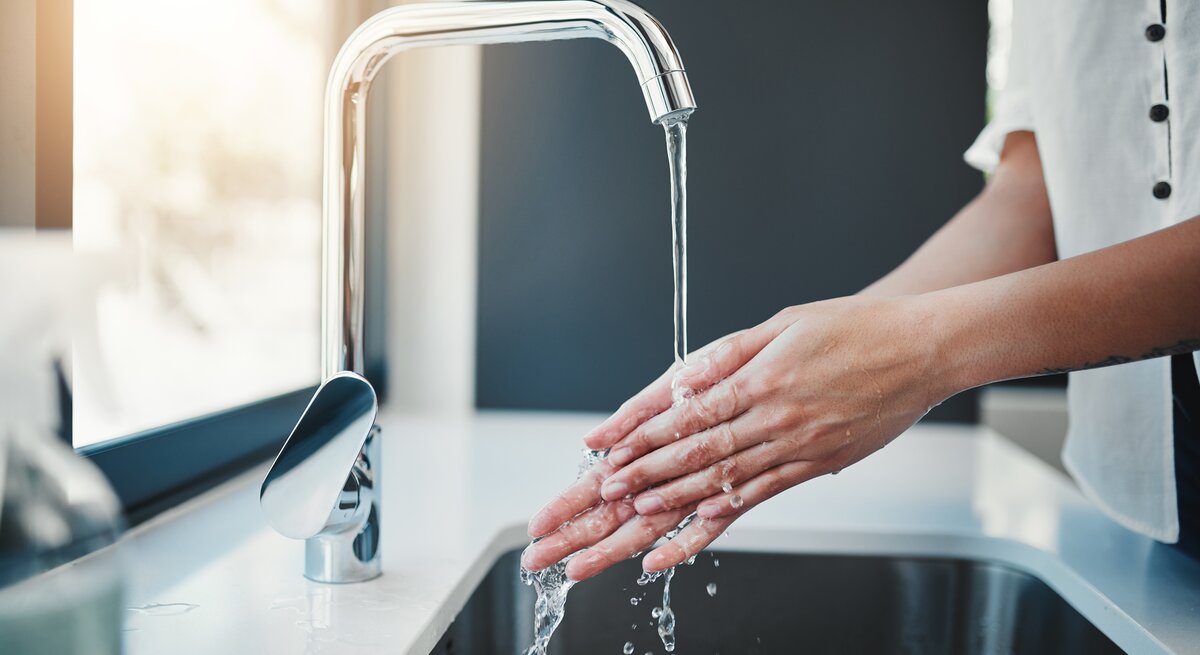 Eine Person wäscht sich sorgfältig die Hände mit Wasser aus einem modernen Wasserhahn über einem Küchenspülbecken.
