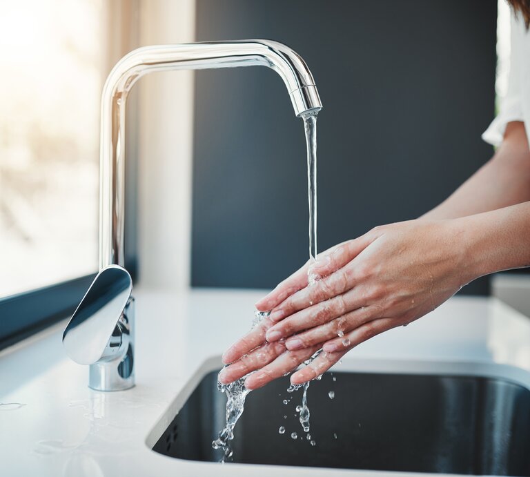 Eine Person wäscht sich sorgfältig die Hände mit Wasser aus einem modernen Wasserhahn über einem Küchenspülbecken. | © iStockphoto.com/Jay Yuno