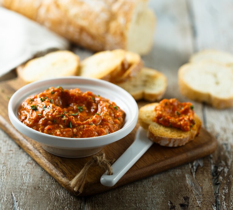Eine Schale Tomate-Walnuss-Aufstrich auf einem Brett, daneben Baguettescheiben. | © Shutterstock/ MariaKovaleva