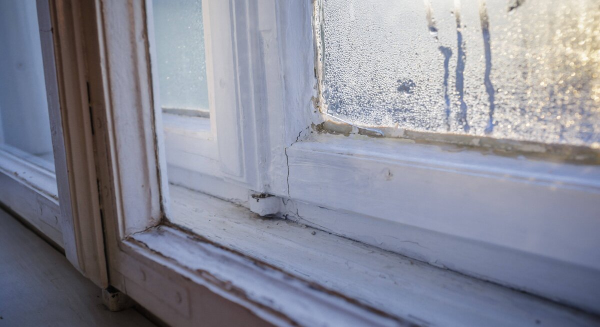Close-up von einer Ecke der Fensterscheibe, in der sich Kondenswasser gebildet hat und die Scheibe hinunterläuft.
