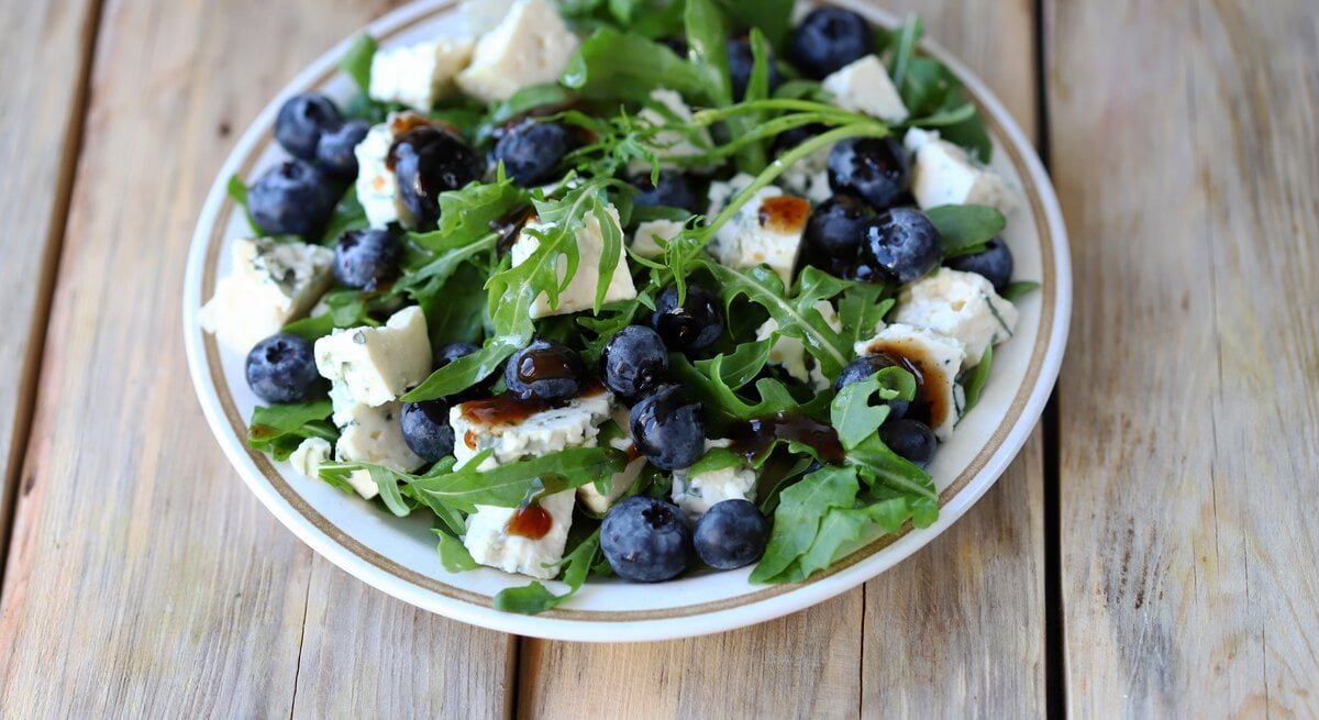 runder Teller / Rucola-Salat mit Feta und Blaubeeren / Untergrund Holz / Draufsicht / nahaufnahme