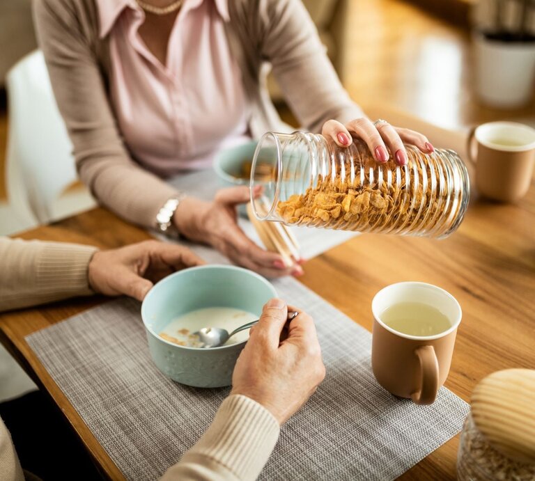 Eine Frau schüttet ihrem Mann am Frühstückstisch Cornflakes in eine Schale | © iStock.com/Drazen Zigic