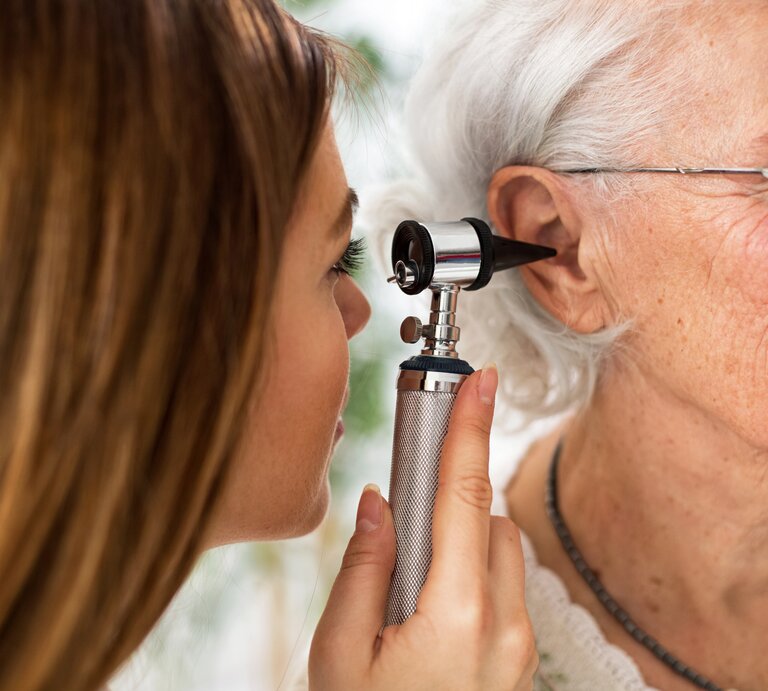 Eine junge Ohrenärztin schaut einer älteren Patientin mit einem Instrument ins Ohr, um zu prüfen, ob sich Eiter gesammelt hat. | © iStock/didesign021