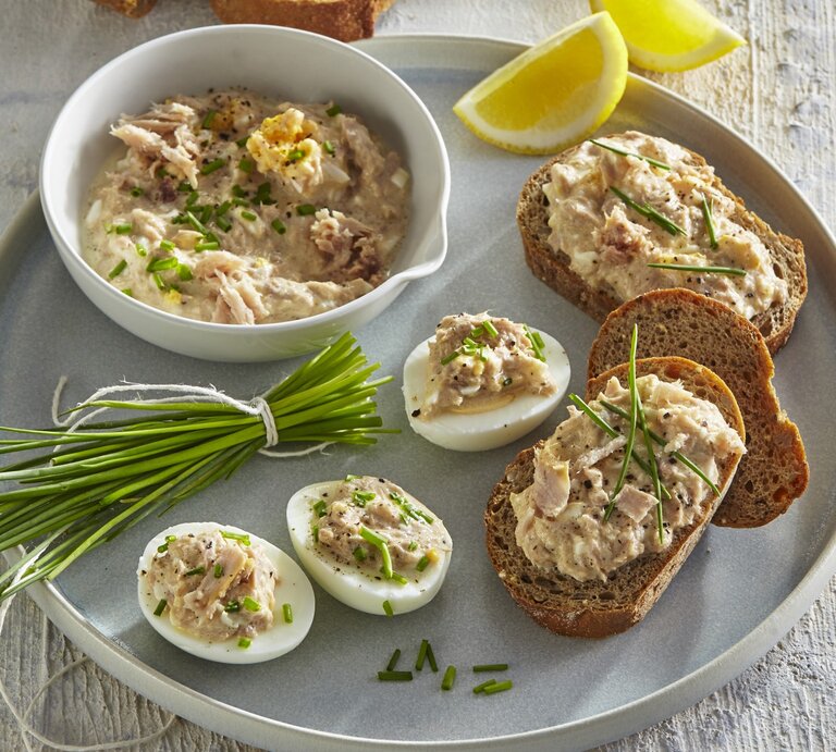 Thunfisch-Ei-Aufstrich in einer Schale und auf Brot und Ei. Daneben liegt Schnittlauch und geschnittene Zitrone.  | © StockFood / Profimedia