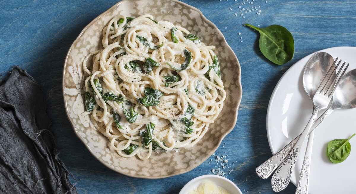 Spaghetti in Spinat-Schmand-Soße auf gewelltem Teller auf blauem Untergrund. 