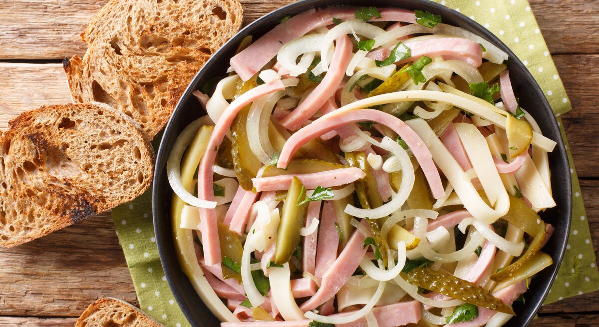 Vogelpersektive: In einer Schüssel ist ein Schweizer Wurstsalat . Daneben lieben drei Scheibe Brot.