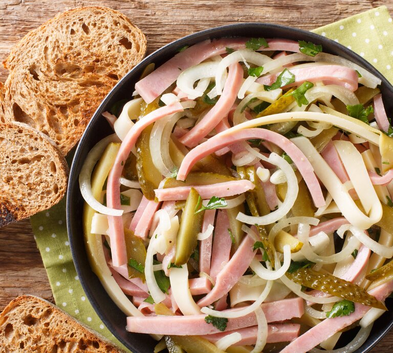 Vogelpersektive: In einer Schüssel ist ein Schweizer Wurstsalat . Daneben lieben drei Scheibe Brot. | © Getty Images / FomaA