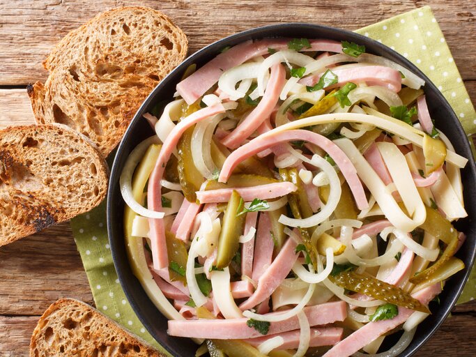 Vogelpersektive: In einer Schüssel ist ein Schweizer Wurstsalat . Daneben lieben drei Scheibe Brot. | © Getty Images / FomaA