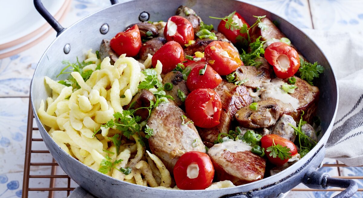 Spätzle-Jägerpfanne mit Pilzen, gerösteter Papika und frischer Petersilie, serviert in einer rustikalen tiefen Pfanne auf einem Keramiktisch. 