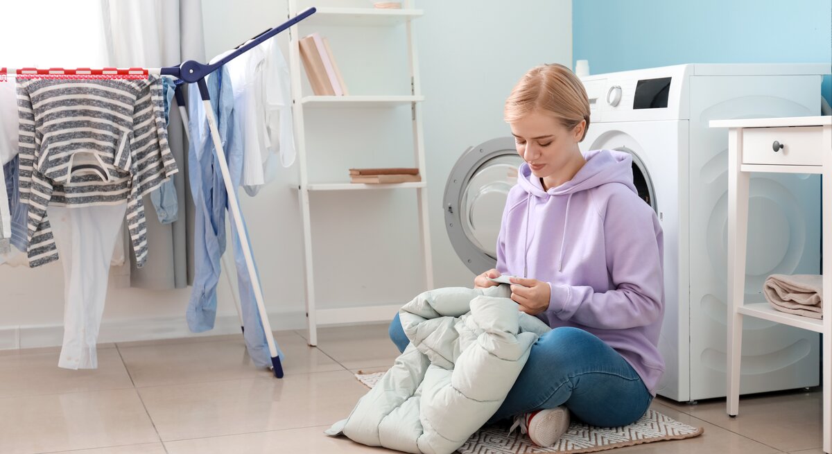 Eine Frau sitzt mit Ihrer Winterjacke auf dem Schoß vor der Waschmaschine und liest das Etikett.