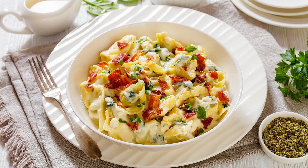 Die Tortellini auf einem weißen Teller. Daneben Kräuter und weißes Geschirr.