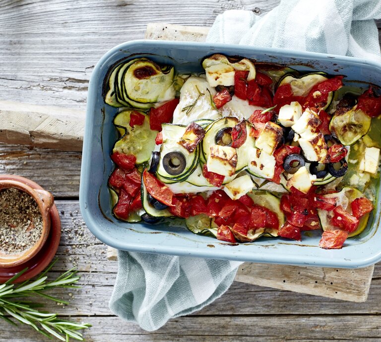 Mediterraner Fischauflauf in einer blauen Auflaufform. Daneben liegen Gewürze, Das Ganze auf einem hölzernen Untergrund.  | © EAT CLUB / Isabell Triemer