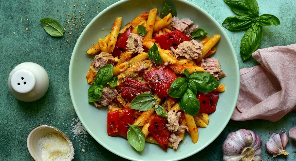 Ein grüner Teller mit der Penne an Thunfisch-Tomatensoße auf einem grünen Untergrund. 