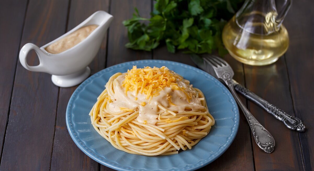 EIn Teller mit Pasta mit Schmelzkäse-Zitronensoße auf einem Holztisch.
