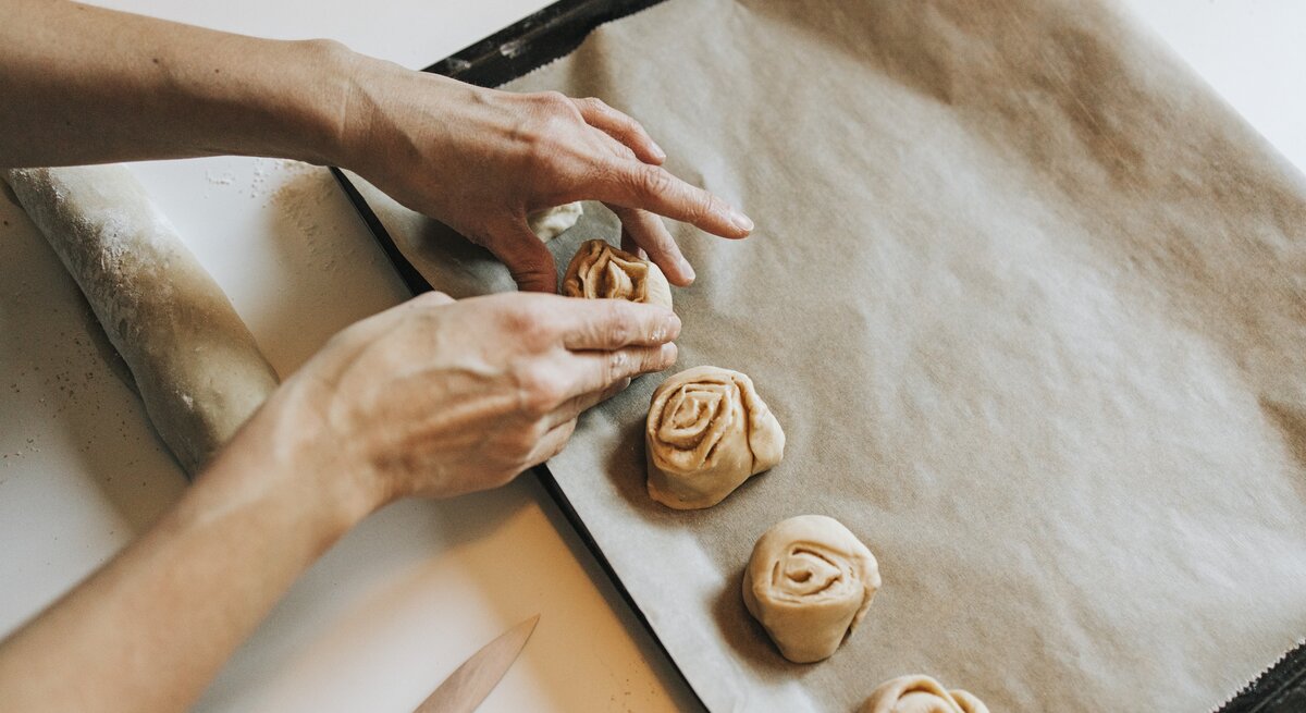 Person drapiert ungebackene Zimtschnecken auf einem Blech mit Backpapier.