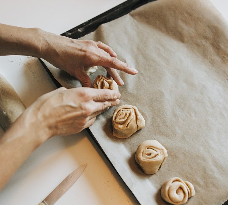 Person drapiert ungebackene Zimtschnecken auf einem Blech mit Backpapier. | © Getty Images/Westend61