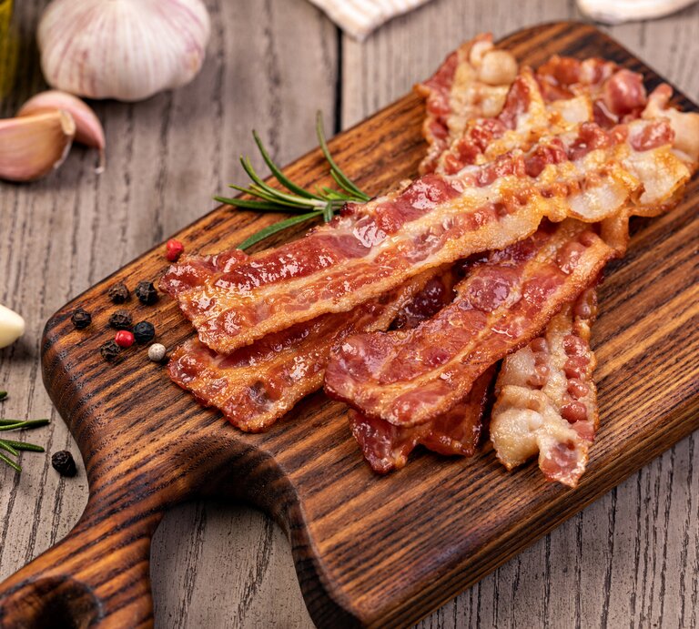 Knuspriger Bacon auf dem Holzbrett von oben fotografiert. | © GettyImages/gresei