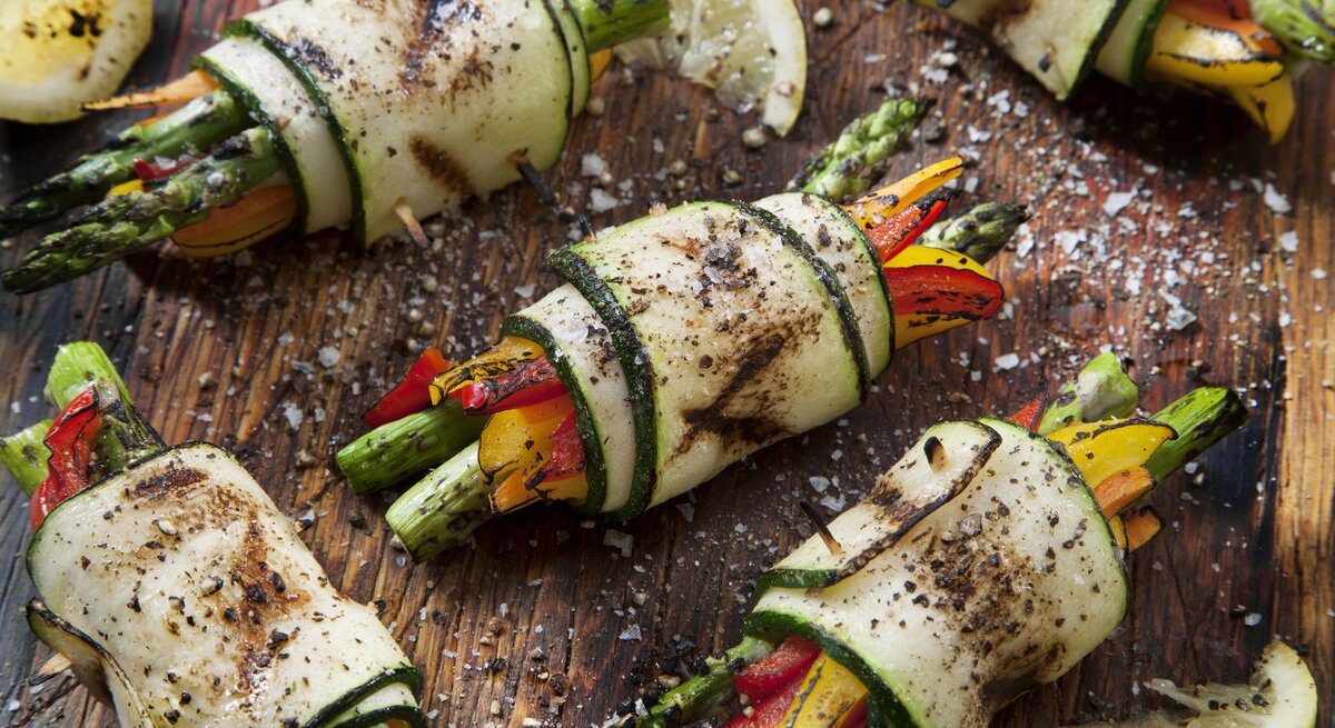 Holzbrett belegt mit Zucchini-Röllchen mit Spargel und Paprika, bestreut mit Meersalz und frischem Pfeffer. 