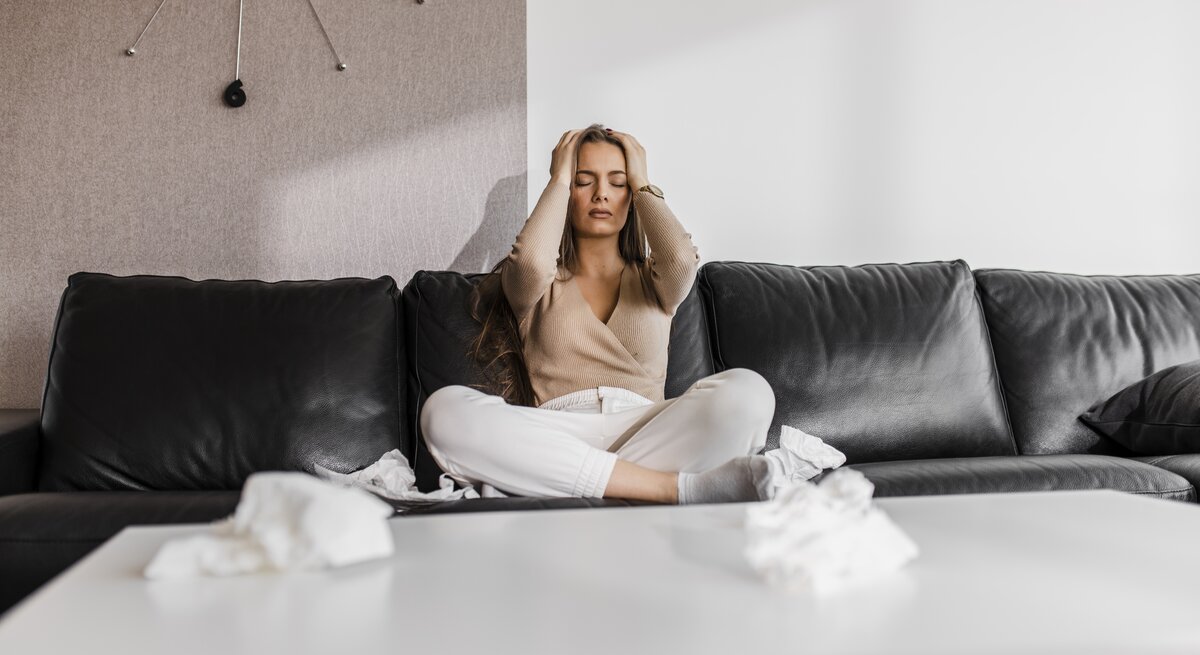 Frau sitzt mit Händen am Kopf auf Sofa