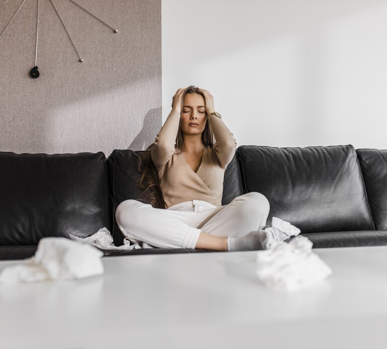 Frau sitzt mit Händen am Kopf auf Sofa | © Getty Images/DjordjeDjurdjevic
