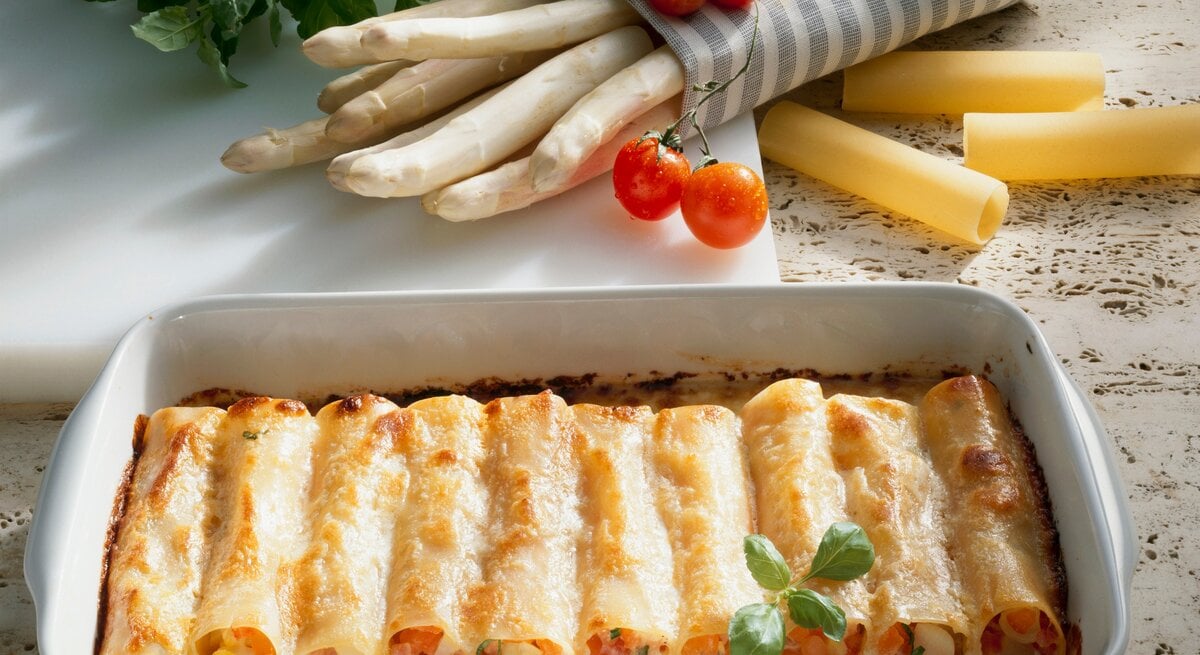 Spargel-Cannelloni in weißer Auflaufform. Daneben einige Zutaten.