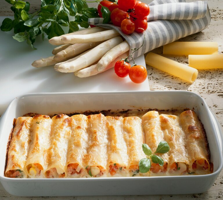 Spargel-Cannelloni in weißer Auflaufform. Daneben einige Zutaten. | © Adobe Stock/superfood