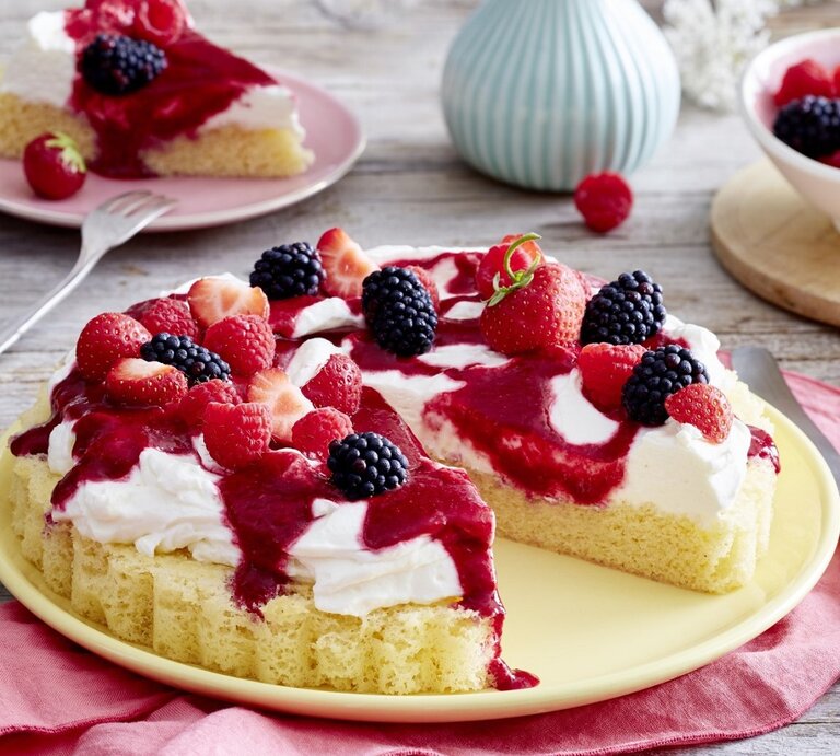 Auf einem Teller steht ein angeschnittener Schmand-Obstkuchen. Er ist mit Himbeersauce und Beeren überzogen.  | © Eat Club / Isabell Triemer