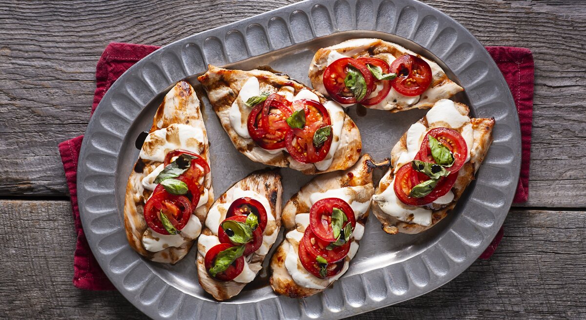 Hähnchen überbacken mit Tomate und Mozzarella auf Servierteller.