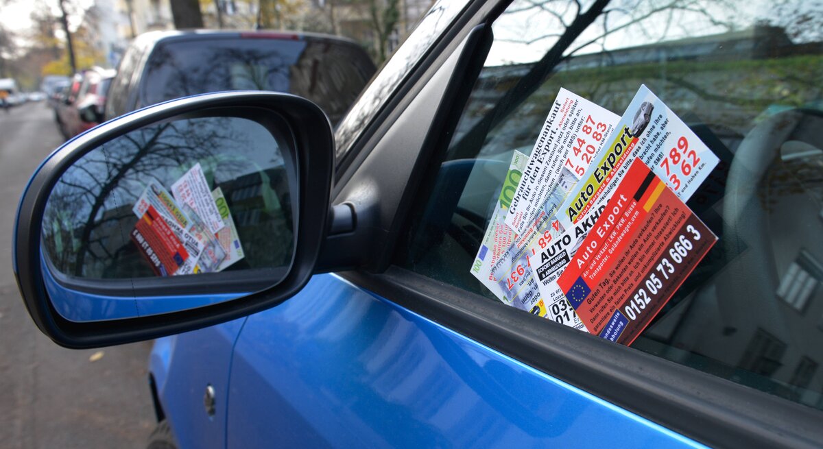 Geparktes, blaues Auto mit Ankaufkarten an der Scheibe.