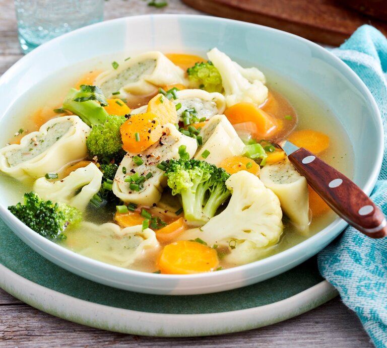 Weiße Schüssel mit Gemüsetopf mit Maultaschen und Löffel vor Holzhintergrund.  | © EAT CLUB / Isabell Triemer