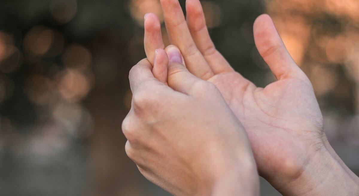 Zwei Hände sind zu sehen. Die rechte Hand massiert die Innenseite des linken Ringfingers, der Schmerzen zu verursachen scheint, was beim paroxysmale Fingerhämatom üblich ist. Der Hintergrund ist unscharf.