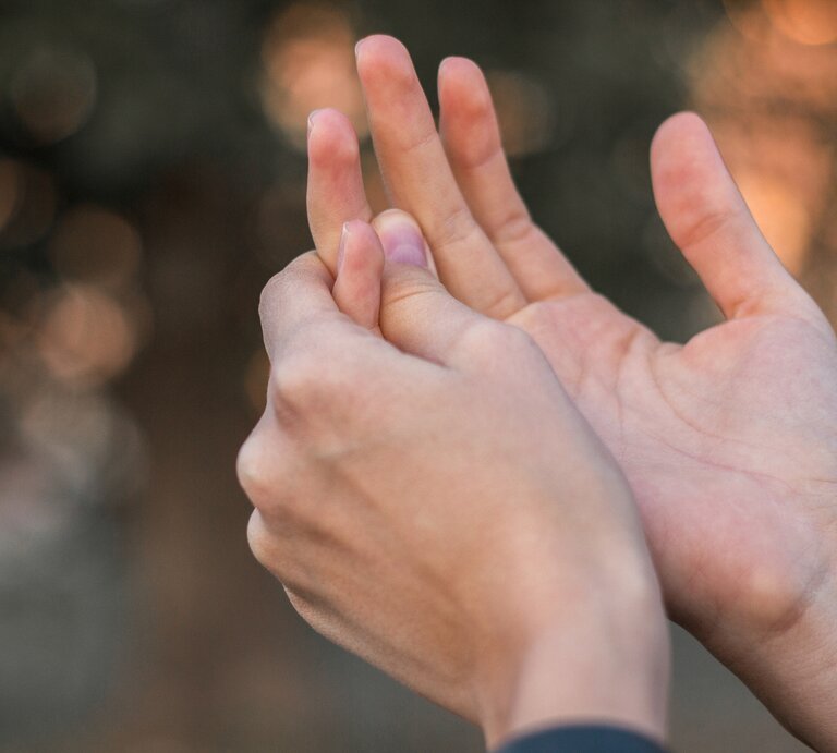 Zwei Hände sind zu sehen. Die rechte Hand massiert die Innenseite des linken Ringfingers, der Schmerzen zu verursachen scheint, was beim paroxysmale Fingerhämatom üblich ist. Der Hintergrund ist unscharf. | © iStock.com/anjagrujic