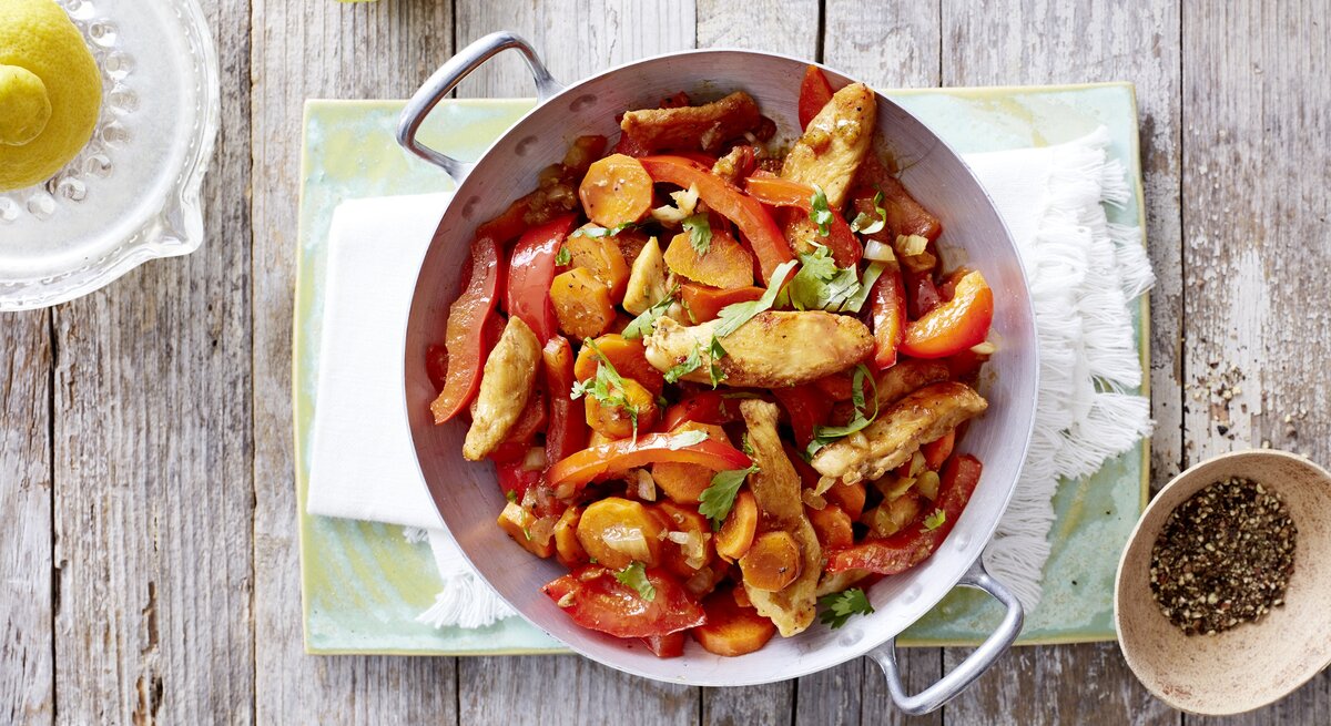 Ein schneller Hähnchen-Wok mit sautiertem Gemüse, abgelöscht mit Sojasauce und garniert mit frischem Koriander und Zitronensaft, serviert im Wok auf einem hellen Holztisch. 
