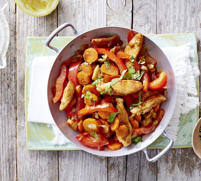 Ein schneller Hähnchen-Wok mit sautiertem Gemüse, abgelöscht mit Sojasauce und garniert mit frischem Koriander und Zitronensaft, serviert im Wok auf einem hellen Holztisch.  | © EAT CLUB/Isabell Triemer