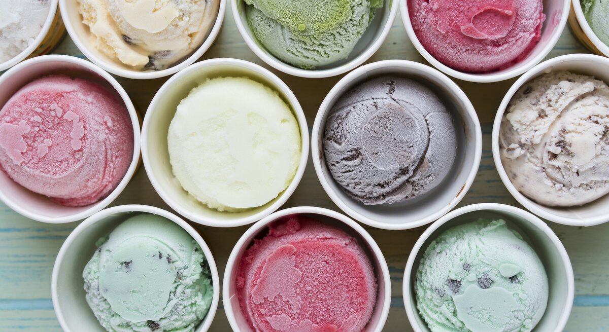 Mehrere bunte Sorten Eis in Pappbechern direkt von oben fotografiert.