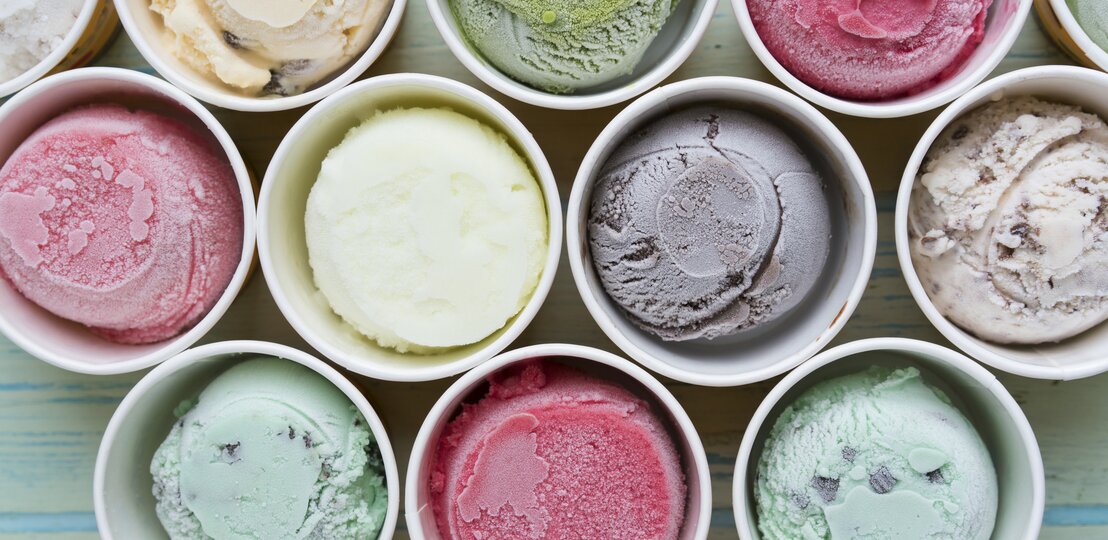 Mehrere bunte Sorten Eis in Pappbechern direkt von oben fotografiert. | © iStock/Tatomm 